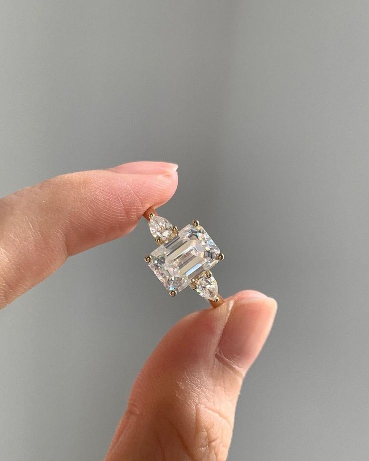 a woman's hand holding an engagement ring with two diamonds on it and the top one in yellow gold