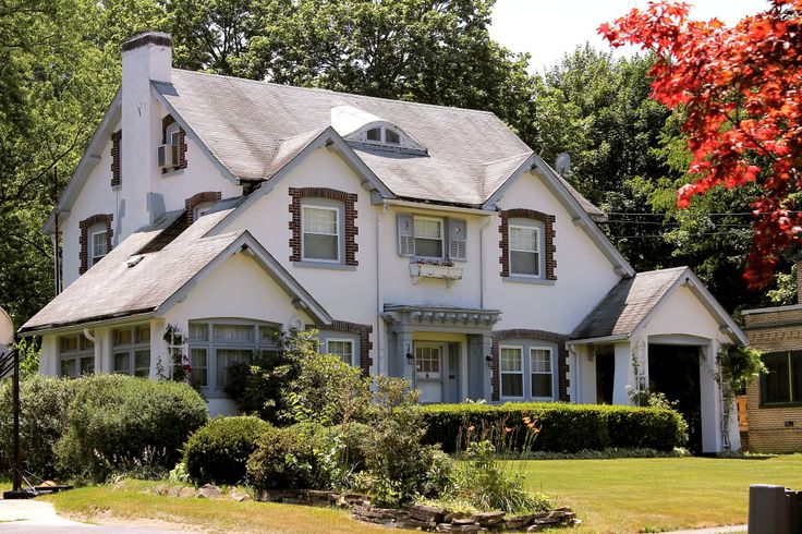 a large white house sitting next to a lush green forest filled with red and orange leaves