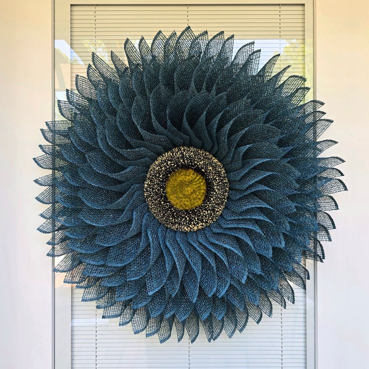 a blue and yellow wreath hanging on the side of a door with blinds behind it