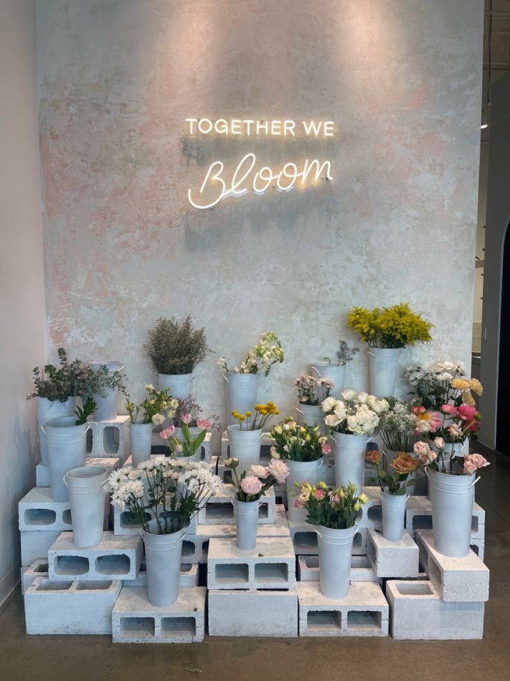 a room filled with lots of white vases and flowers next to a neon sign that reads together we bloom