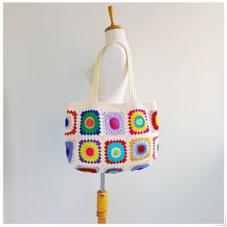 a multicolored crocheted bag hanging on a wooden stand with a white background