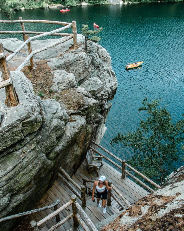 two people are walking up the stairs to a lake that is surrounded by rocky cliffs