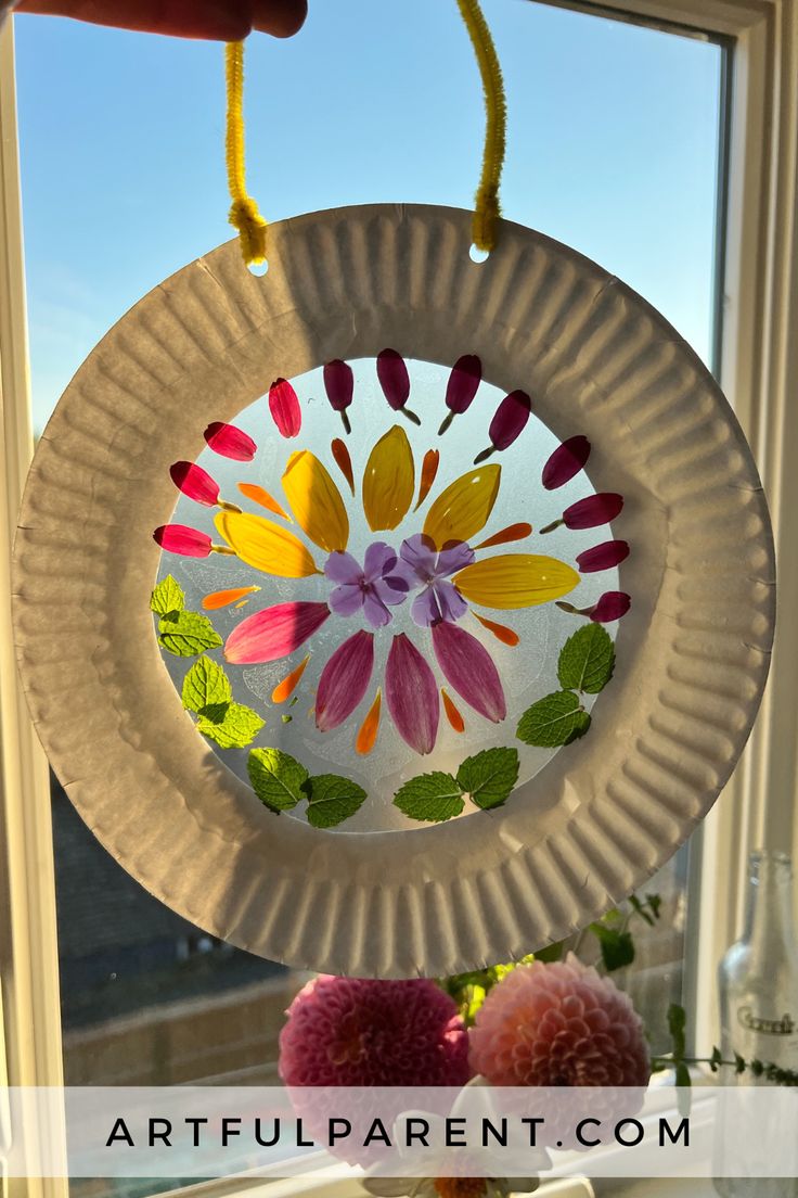 a paper plate with flowers on it hanging from a window sill