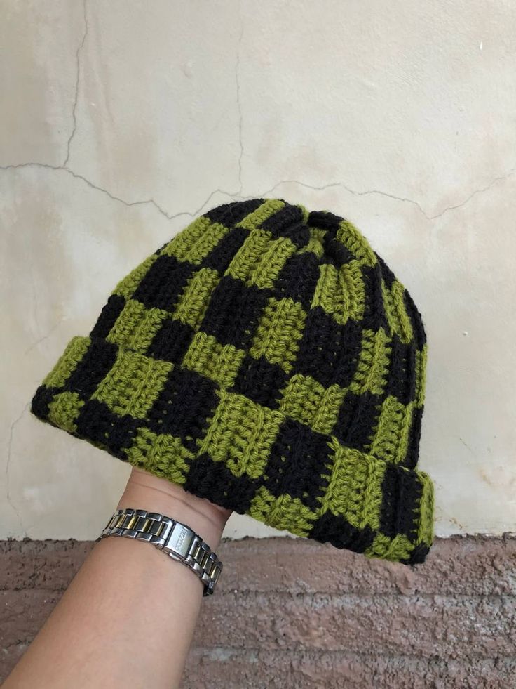 a hand that is wearing a green and black knitted hat