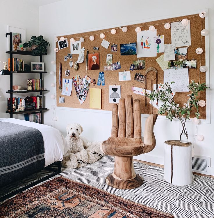 a bedroom with a bed, chair and cork board on the wall that has pictures all over it