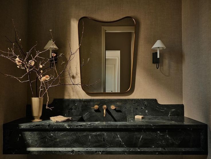 a bathroom sink sitting under a mirror next to a vase with flowers