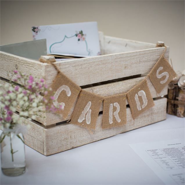 there is a wooden crate with some cards on it and flowers in the vase next to it