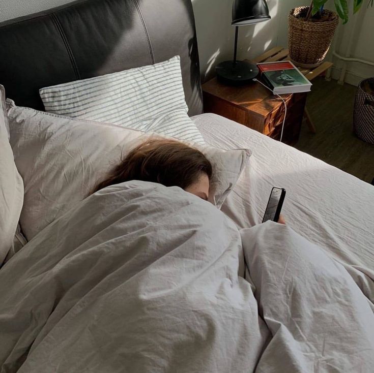 a woman is laying in bed with her head on the pillow and holding a remote control