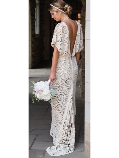 a woman standing in front of a building wearing a white dress and holding a bouquet