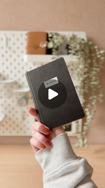 a woman holding up a black book with a video player on it's cover