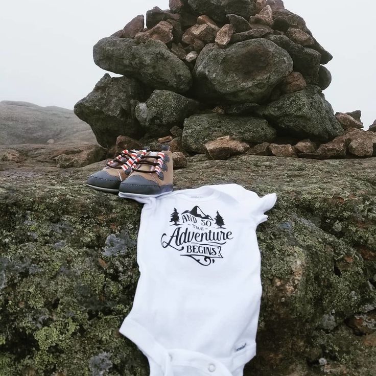 a baby's bodysuit and shoes are sitting on top of a rock formation