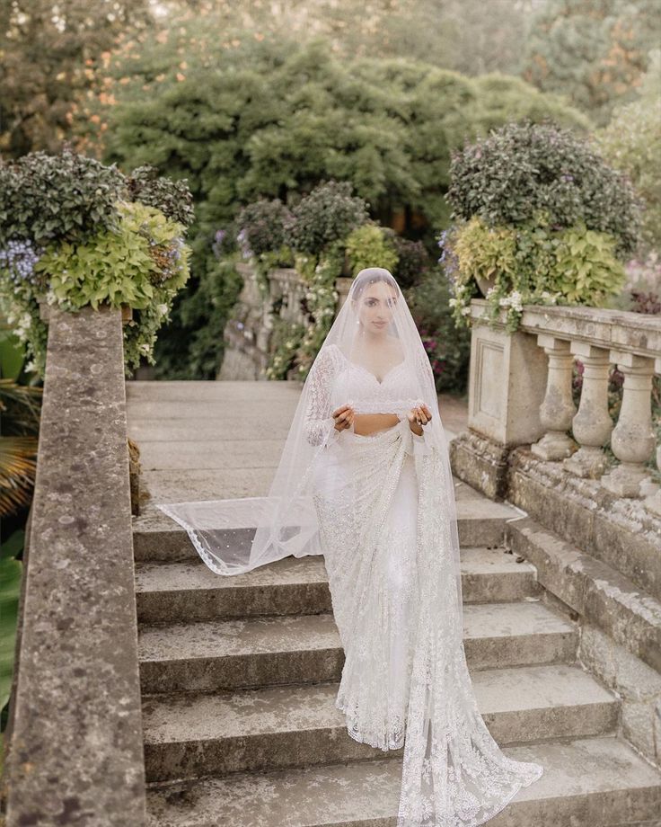 a woman in a white wedding dress standing on some steps with a veil over her head