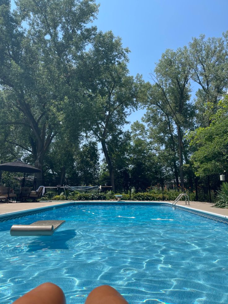 a person's feet in the water next to a swimming pool with trees behind them