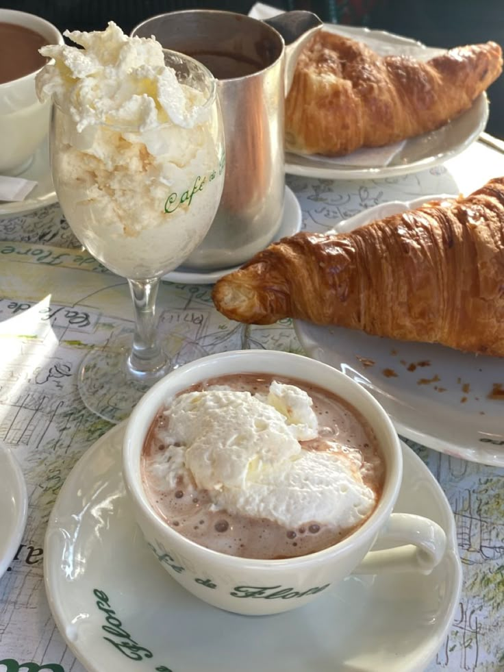 there is a croissant and coffee on the table with other food items around it