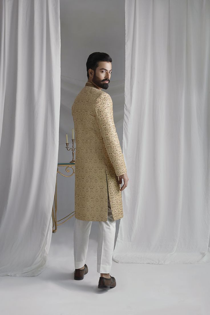 Discover the timeless elegance and regal charm of our Collar Detail Gold Sherwani. Made from pure atlas material, this sherwani features exquisite hand-embroidered jal work of resham, zardozi, Swarovski stones, and dabka. Complete with a jamawar kula (turban) and silk inner kurta pajama, this resplendent piece is perfect for any special occasion. Elevate your style with this luxurious and sophisticated sherwani. 4-Piece Suit Elegant Sherwani In Raw Silk With Straight Kurta, Elegant Raw Silk Sherwani Straight Kurta, Elegant Bandhgala With Naqshi In Raw Silk, Elegant Raw Silk Bandhgala With Naqshi, Gold Sherwani With Zari Work For Transitional Season, Gold Sherwani With Resham Embroidery And Kundan, Elegant Raw Silk Sherwani With Dabka Detailing, Gold Naqshi Unstitched Straight Kurta Suit, Elegant Designer Wear Sherwani With Straight Kurta