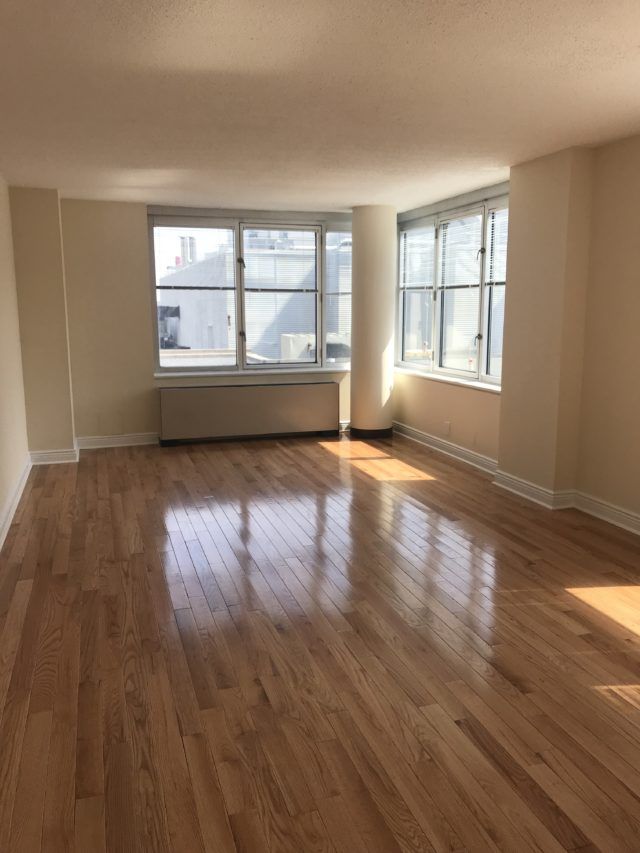 an empty room with hard wood flooring and large windows in the corner on one side