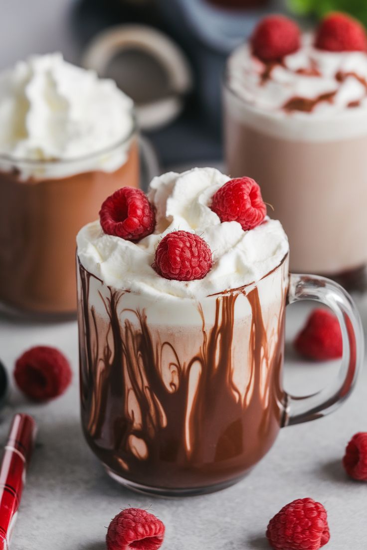 two mugs filled with chocolate and raspberries on top of a table next to some whipped cream