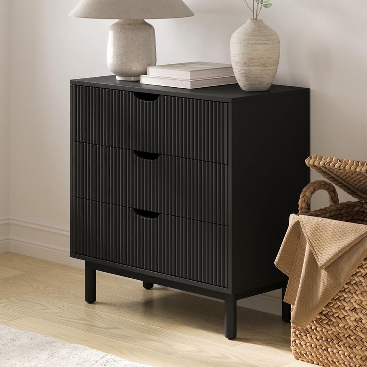 a black cabinet with three drawers next to a lamp and wicker basket on the floor