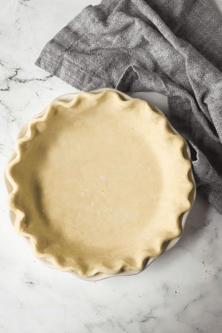 an uncooked pie crust sitting on top of a white counter next to a gray napkin