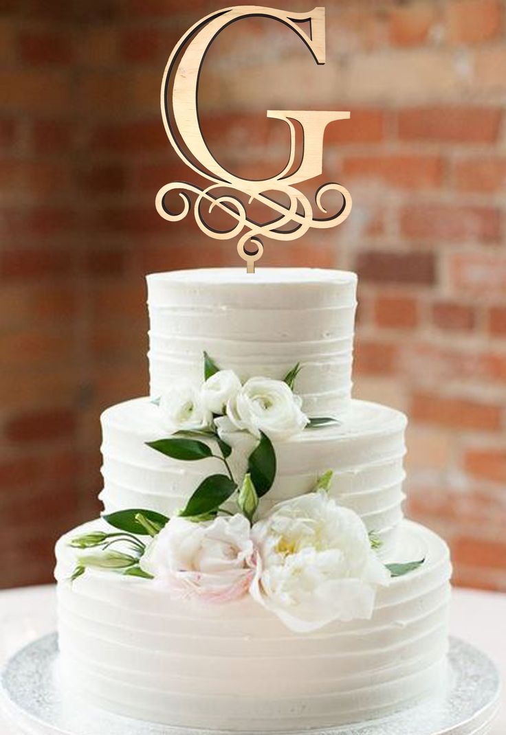 a wedding cake with white flowers and the letter g on top