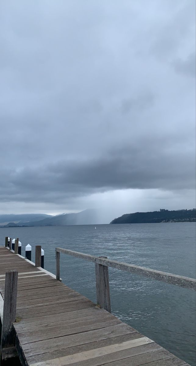 a wooden dock with water and clouds in the background