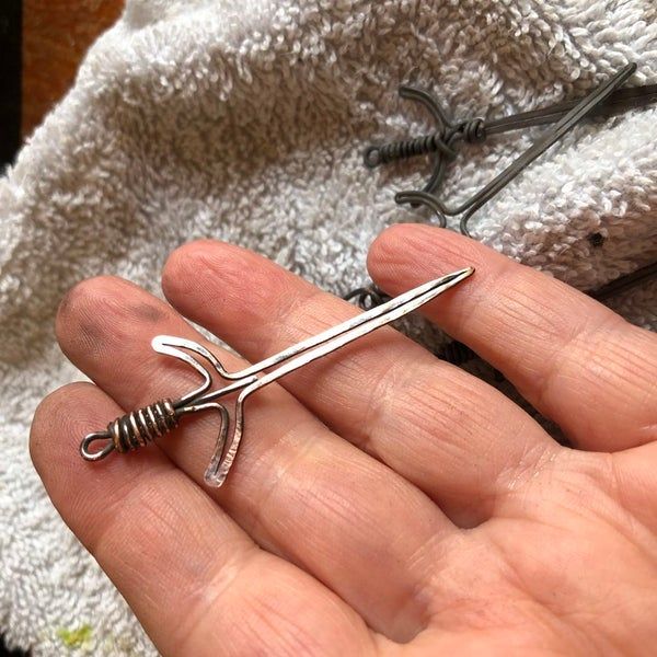 a hand holding a pair of scissors on top of a towel next to some nails