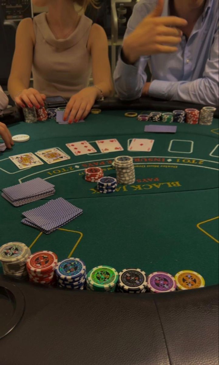 two people sitting at a table with cards and chips in front of them on the table