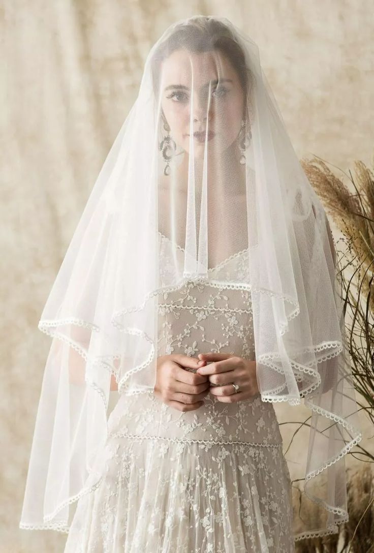 a woman in a wedding dress with a veil over her head and flowers behind her