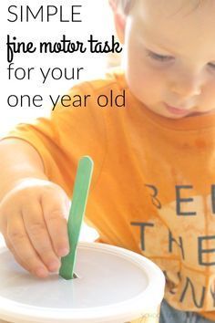 a young boy holding a plastic cup with a green stick sticking out of it and the words simple fine motor task for your one year old