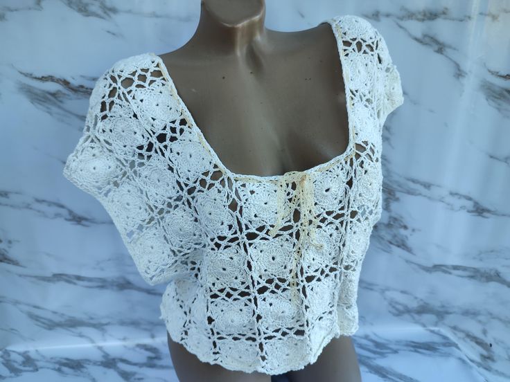 a mannequin wearing a white crochet top on a marble display case