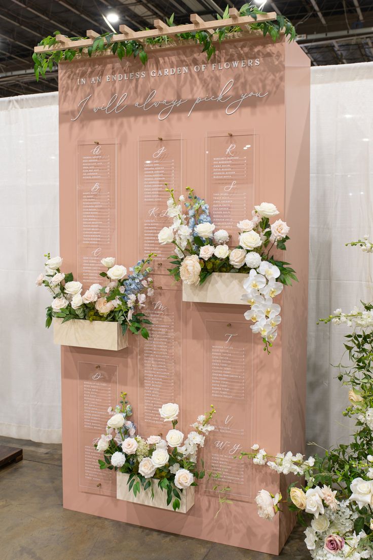 a pink wall with flowers and greenery on the sides, along with seating cards