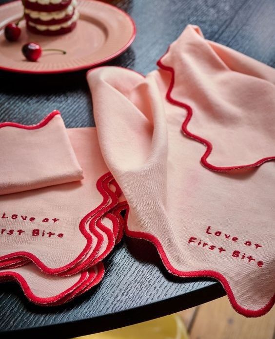 two napkins with embroidered words on them sitting on a table next to a piece of cake