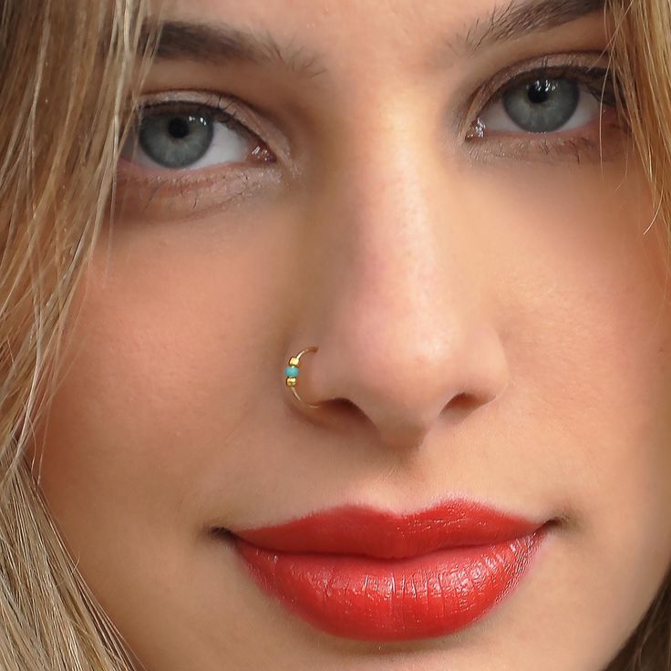 a close up of a woman with red lipstick and piercing on her nose looking at the camera