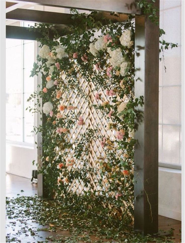 an arrangement of flowers and greenery is displayed on the wall behind a wooden trellis