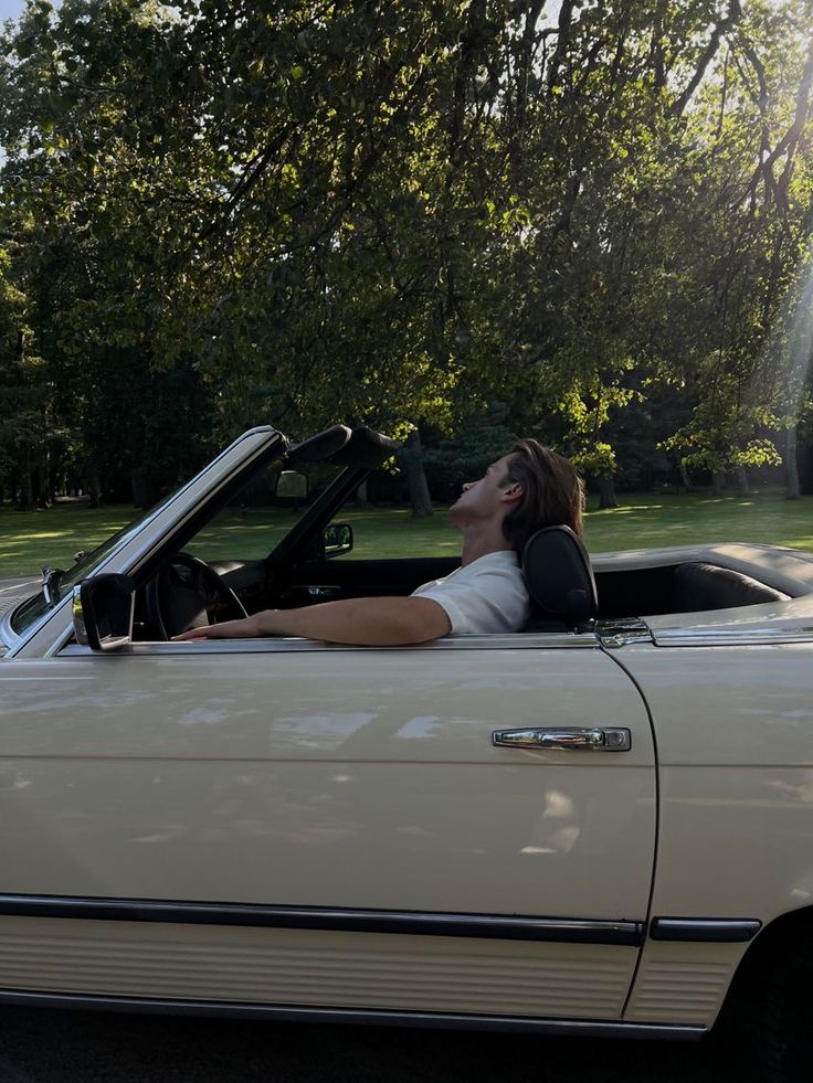 a woman sitting in the driver's seat of a convertible car with her eyes closed