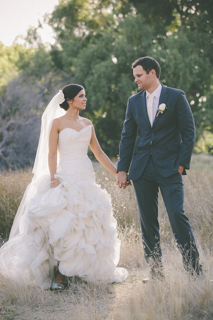 a bride and groom holding hands walking through tall grass