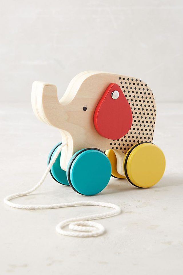 a wooden toy elephant with colorful wheels on a white surface, next to a string