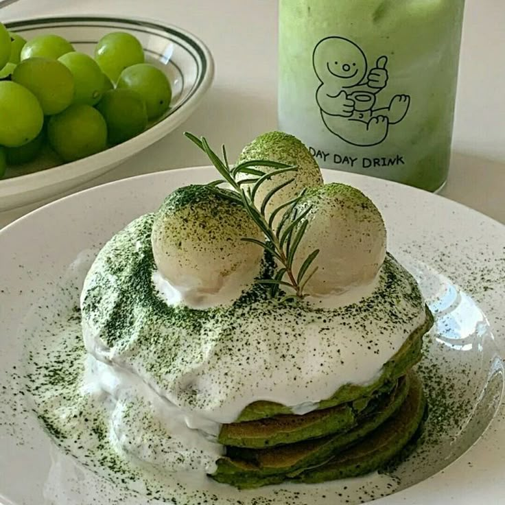 a stack of green pancakes with whipped cream and sprinkles on top, next to a bowl of grapes