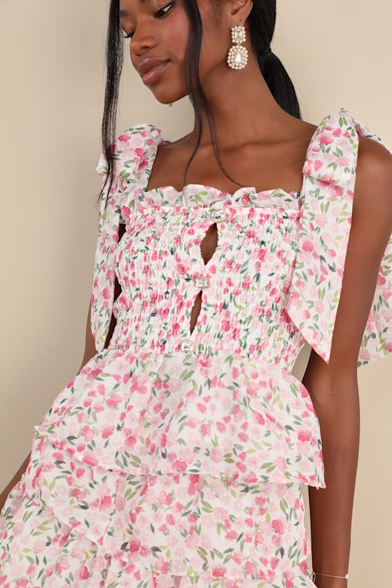 With flirty and femme vibes galore, we can't get enough of the Sister Jane Wild Hearts Ivory Multi Floral Smocked Tie-Strap Tank Top! Lightweight woven fabric features a romantic floral print as it shapes tying straps that support a smocked bodice with a straight neckline, ruffled trim, and a faux button placket at the front with rhinestone buttons and cutout details. Ruffled, peplum-style hem completes the look. Pair with the matching skirt for a complete look! Fit: This garment fits true to si Fitted Flirty Smocked Top For Day Out, Spring Fitted Flirty Smocked Top, Fitted Smocked Top For Spring, Flirty Style, Fitted Smocked Top In Flirty Style For Spring, Flirty Smocked Top For Brunch, Fitted Flirty Smocked Top For Spring, Feminine Smocked Top For Brunch, Chic Smocked Top With Elastic Neckline For Vacation, Flirty Smocked Bodice Top For Day Out