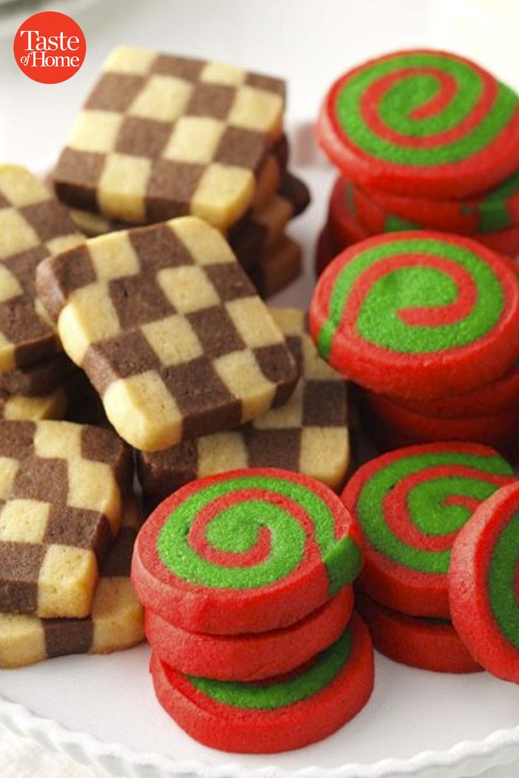 some red and green cookies are on a white plate next to other small ones in the shape of checkered squares