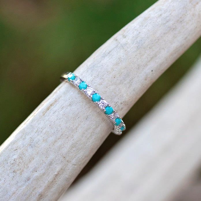 a white gold ring with blue stones on it sitting on a piece of drift wood