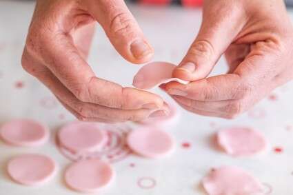 two hands are holding something in front of some pink circles on a white counter top