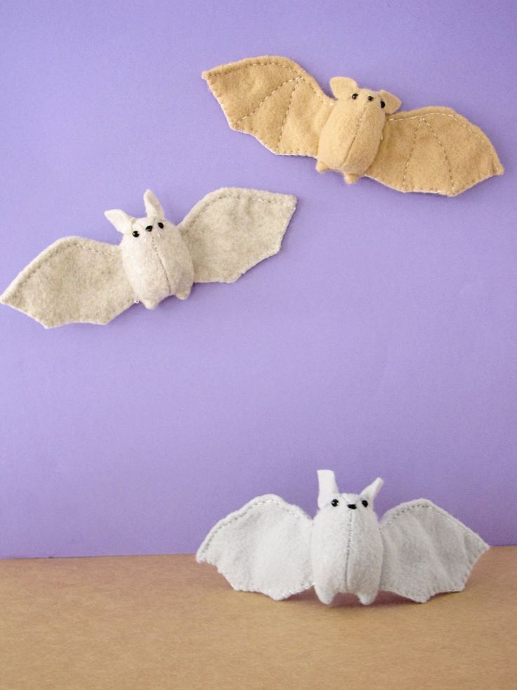 three felt bats on a purple background with one white bat and the other yellow bat