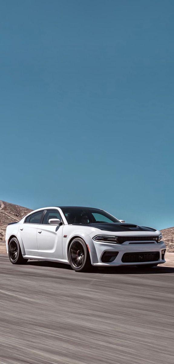 the white dodge charger driving on a road with mountains in the background and blue sky