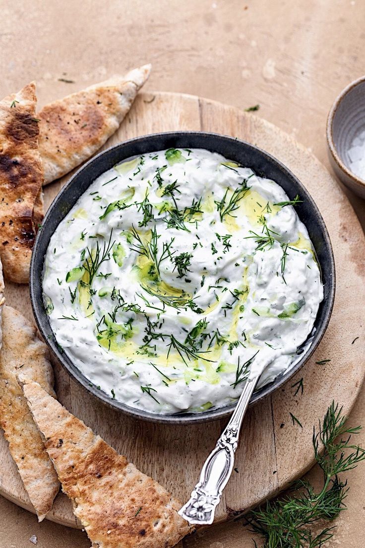 a bowl of dip with pita bread and dill on the side next to it