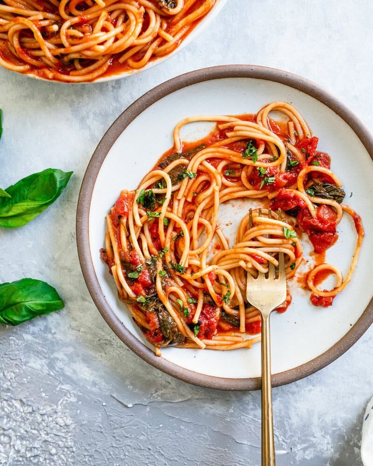 a white plate topped with pasta and sauce next to a bowl of spinach leaves