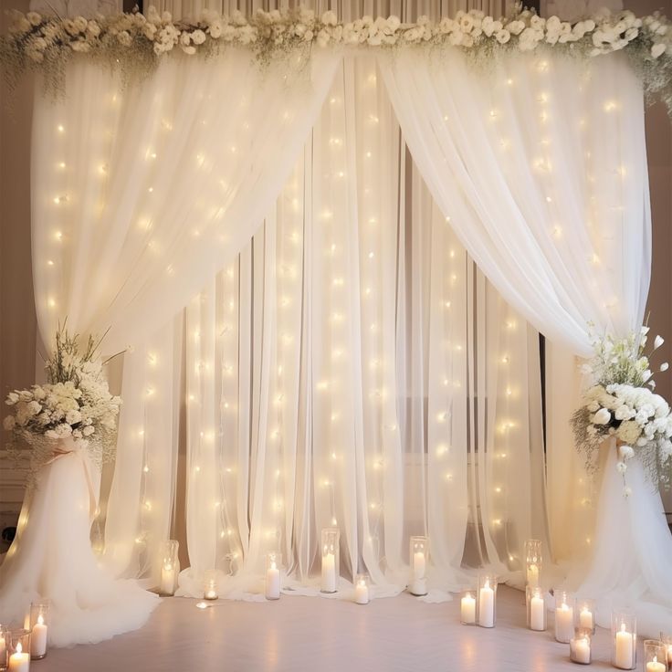 a wedding stage decorated with white flowers, candles and sheer draping for the backdrop