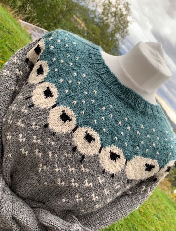 a knitted sweater with white and black balls on it, sitting in the grass