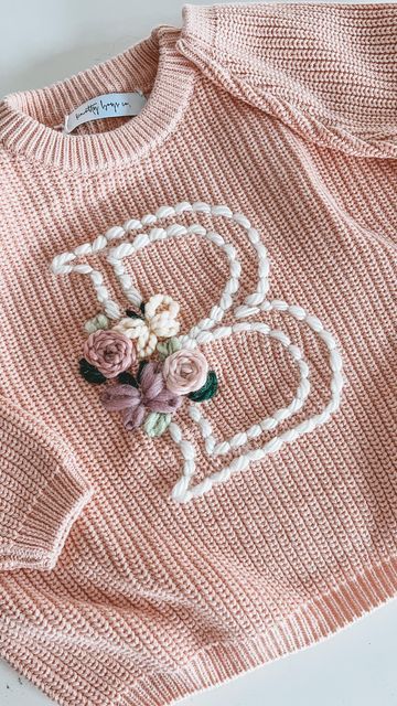 a pink sweater with flowers on it and a heart embroidered on the front, sitting on a white surface