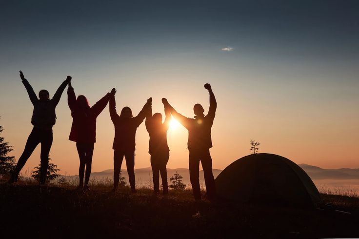 group of people standing on top of a hill with their arms in the air at sunset